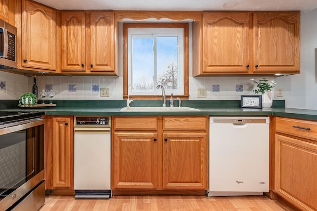 kitchen featuring dark countertops, appliances with stainless steel finishes, light wood-style floors, and a sink