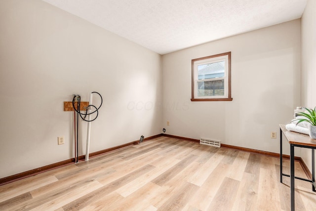 spare room featuring a textured ceiling, baseboards, visible vents, and light wood-type flooring