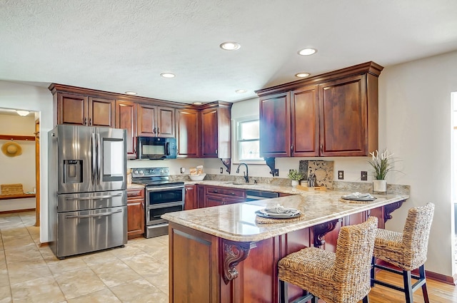 kitchen featuring a kitchen bar, sink, stainless steel appliances, kitchen peninsula, and light stone countertops