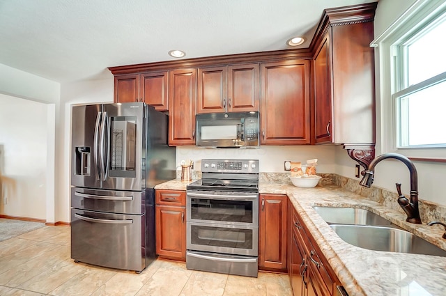 kitchen with appliances with stainless steel finishes, sink, and light stone counters