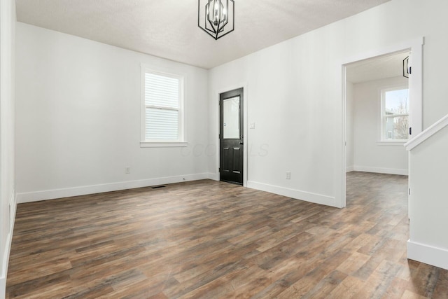 spare room with a textured ceiling, a chandelier, and dark hardwood / wood-style flooring