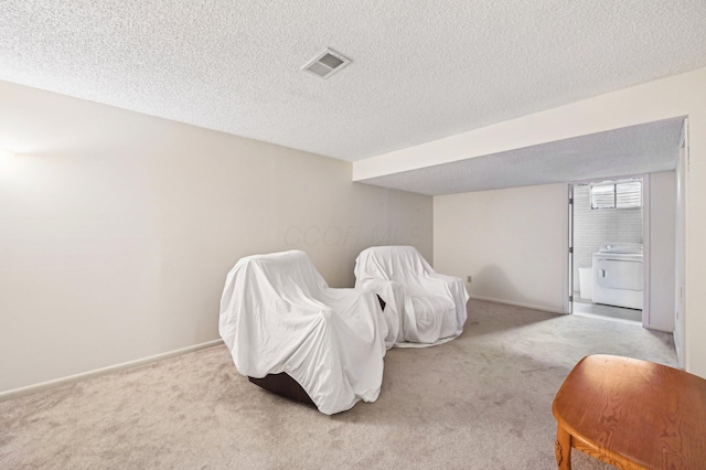 bedroom featuring a textured ceiling, washer / clothes dryer, and light colored carpet