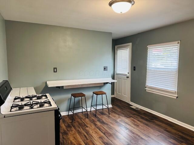 kitchen with dark hardwood / wood-style flooring, kitchen peninsula, a breakfast bar, and white gas stove