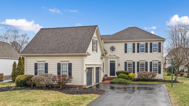 colonial home featuring a front lawn, aphalt driveway, and roof with shingles