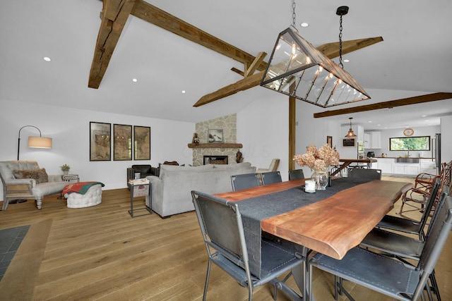 dining area with lofted ceiling with beams, light wood-type flooring, sink, and a fireplace