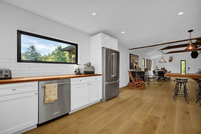 kitchen with white cabinetry, stainless steel appliances, tasteful backsplash, wood counters, and decorative light fixtures