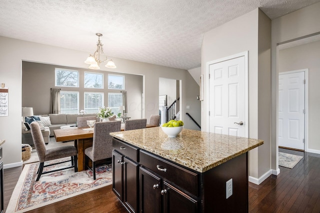 kitchen featuring dark wood-type flooring, dark brown cabinetry, decorative light fixtures, a center island, and light stone countertops