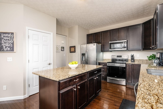 kitchen with dark brown cabinetry, light stone counters, dark hardwood / wood-style flooring, a kitchen island, and stainless steel appliances