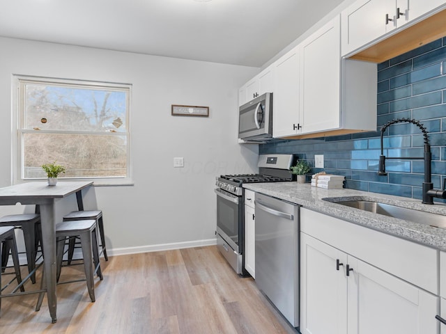 kitchen featuring sink, white cabinetry, light wood-type flooring, appliances with stainless steel finishes, and decorative backsplash