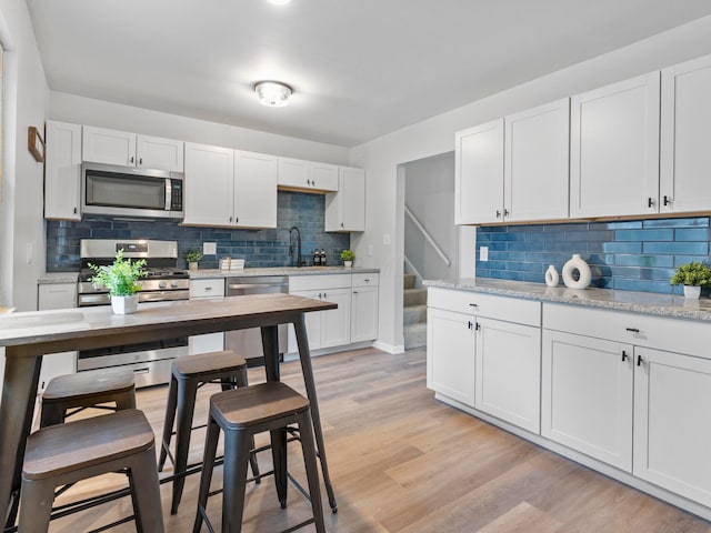 kitchen with white cabinetry, stainless steel appliances, light stone countertops, and light wood-type flooring