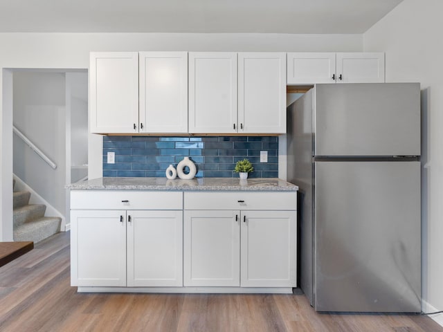 kitchen featuring backsplash, stainless steel fridge, light wood-type flooring, and white cabinets