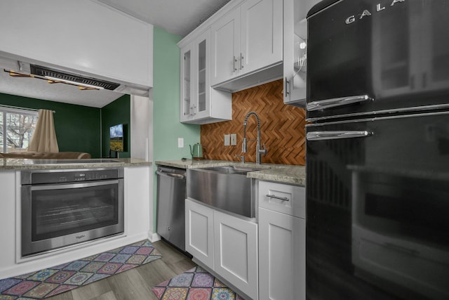 kitchen with white cabinetry, light wood-type flooring, appliances with stainless steel finishes, light stone countertops, and decorative backsplash