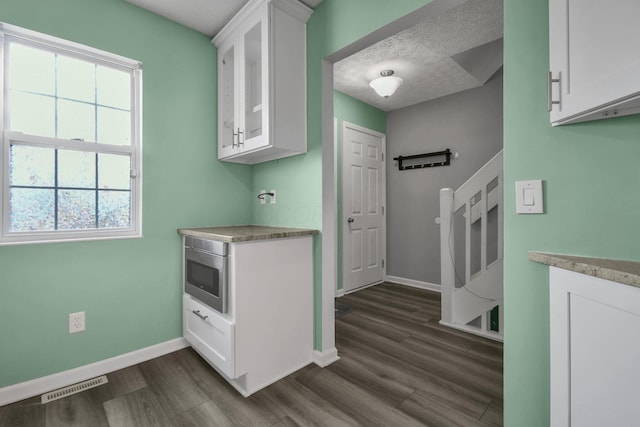 kitchen with a textured ceiling, stainless steel microwave, white cabinets, and dark hardwood / wood-style flooring