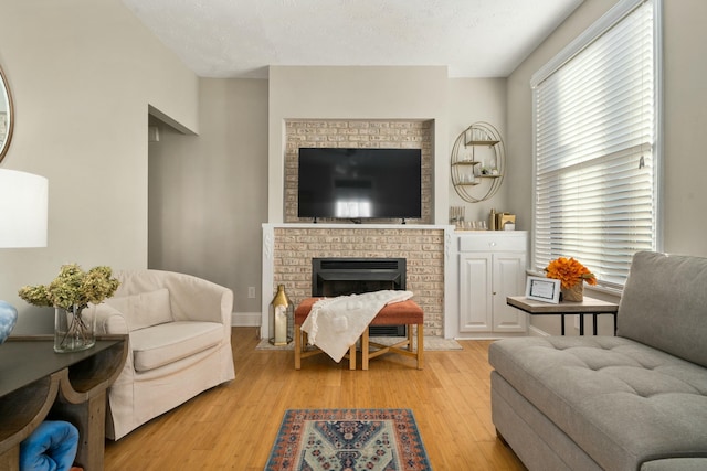 living room with a textured ceiling, a brick fireplace, and light hardwood / wood-style flooring