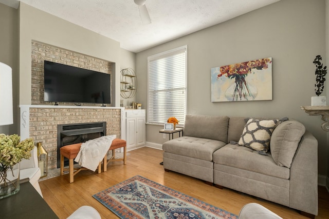 living room with light hardwood / wood-style floors, ceiling fan, a textured ceiling, and a fireplace