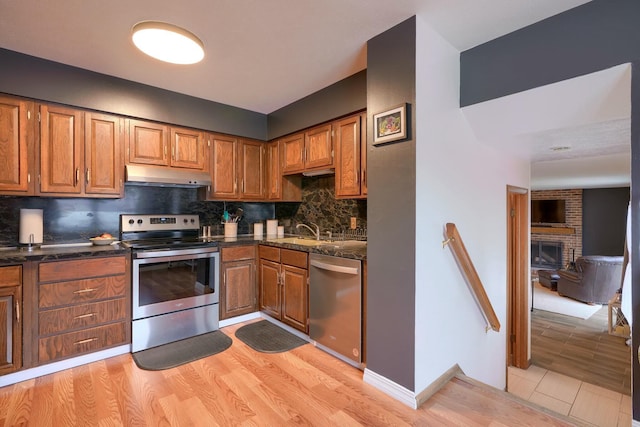 kitchen with sink, stainless steel appliances, a fireplace, light hardwood / wood-style floors, and backsplash