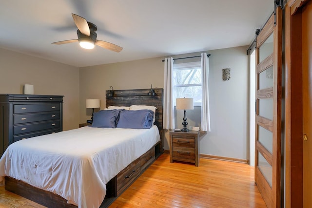 bedroom with a barn door, ceiling fan, and light hardwood / wood-style flooring