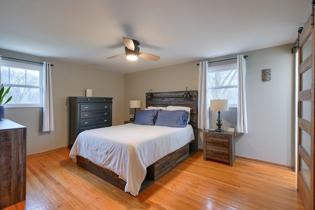 bedroom with multiple windows, light hardwood / wood-style flooring, a barn door, and ceiling fan