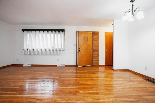 spare room with an inviting chandelier and light hardwood / wood-style floors