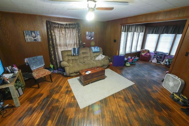 living room featuring dark wood-type flooring, wooden walls, and ceiling fan