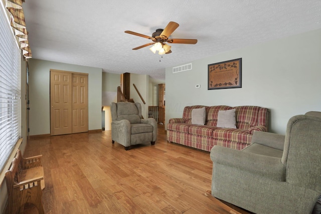 living room featuring visible vents, baseboards, a ceiling fan, a textured ceiling, and light wood-style floors