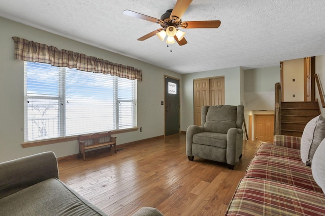 living room featuring light wood-style floors, a textured ceiling, baseboards, and a ceiling fan