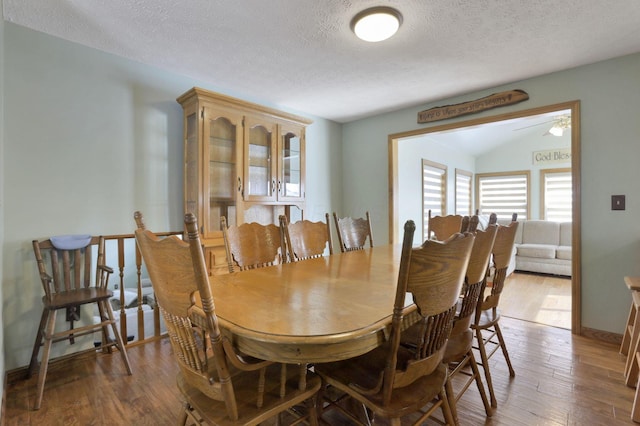 dining area with a textured ceiling, wood finished floors, lofted ceiling, and baseboards