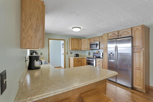 kitchen with a peninsula, stainless steel appliances, light countertops, light brown cabinetry, and light wood-type flooring