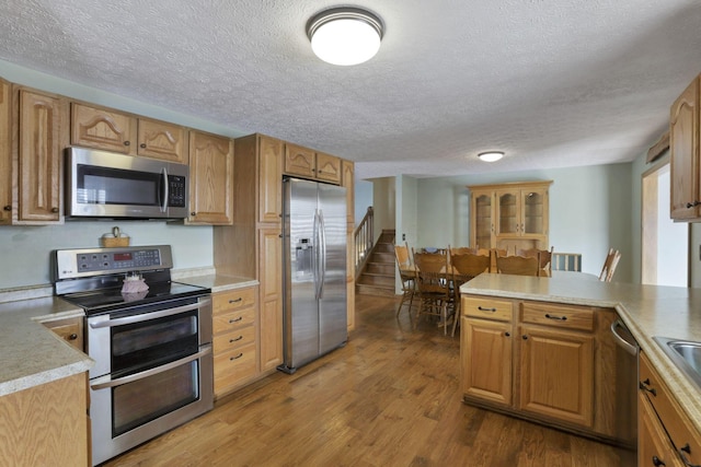 kitchen with a textured ceiling, light countertops, appliances with stainless steel finishes, and wood finished floors