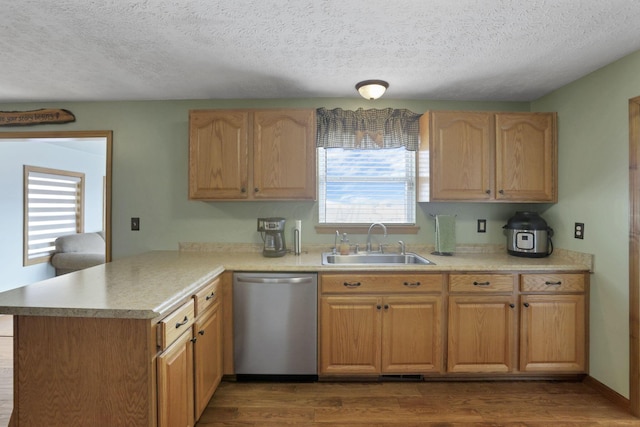 kitchen featuring a peninsula, a sink, a healthy amount of sunlight, light countertops, and stainless steel dishwasher