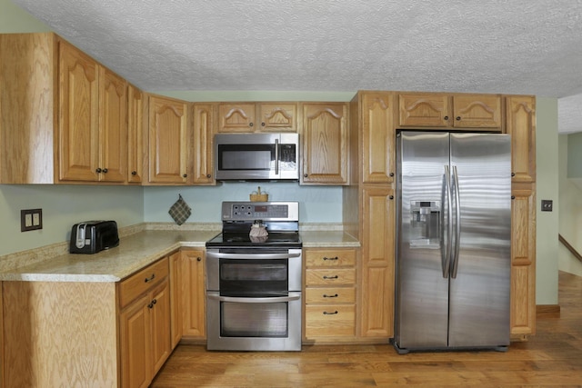 kitchen with light wood finished floors, stainless steel appliances, and a textured ceiling