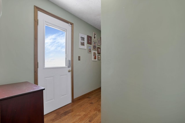 doorway to outside with a textured ceiling and light wood finished floors