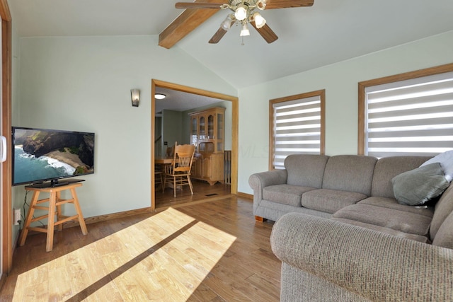 living area featuring lofted ceiling with beams, a ceiling fan, baseboards, and wood finished floors