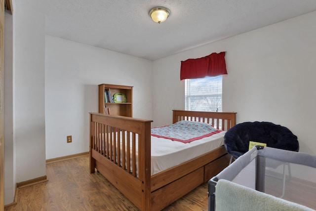 bedroom with a textured ceiling, wood finished floors, and baseboards