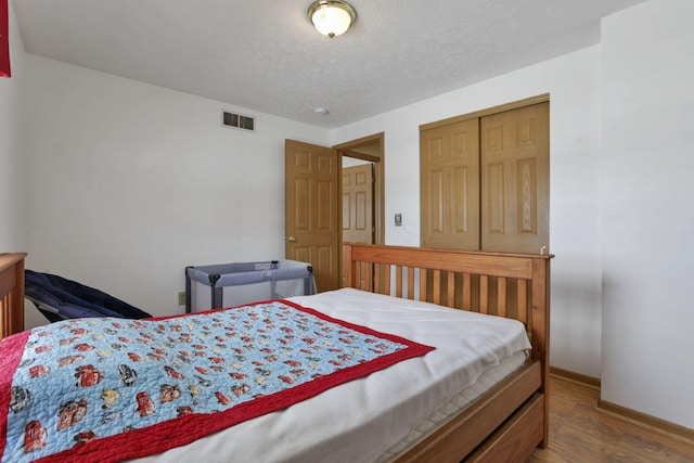 bedroom featuring a textured ceiling, wood finished floors, visible vents, and baseboards