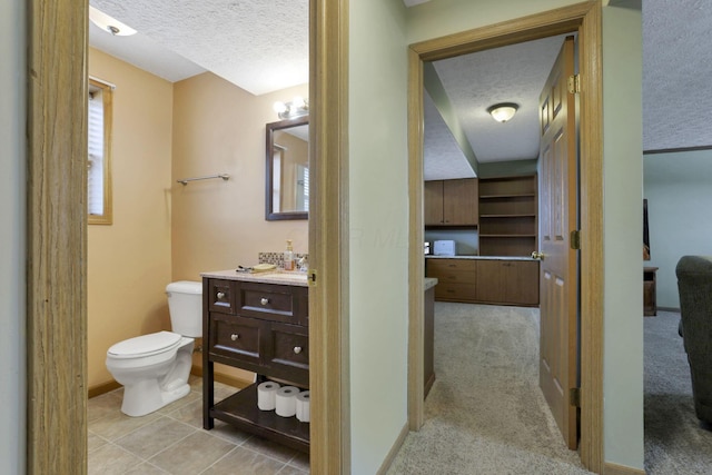 half bath featuring toilet, a textured ceiling, vanity, baseboards, and tile patterned floors