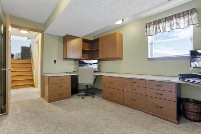 home office featuring built in study area, light carpet, and a textured ceiling