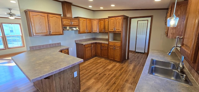 kitchen featuring sink, wood-type flooring, ornamental molding, decorative light fixtures, and kitchen peninsula