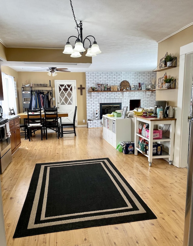 living room featuring light hardwood / wood-style flooring, brick wall, a fireplace, ceiling fan with notable chandelier, and ornamental molding