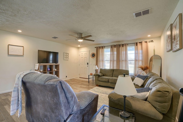 living room with ceiling fan, a textured ceiling, and light wood-type flooring