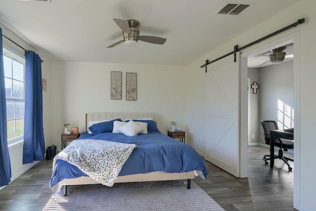 bedroom with ceiling fan, a barn door, and dark hardwood / wood-style flooring