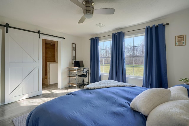 bedroom with ceiling fan, a barn door, and light hardwood / wood-style floors