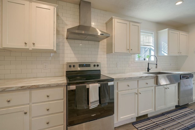 kitchen featuring white cabinetry, appliances with stainless steel finishes, light stone counters, and wall chimney range hood