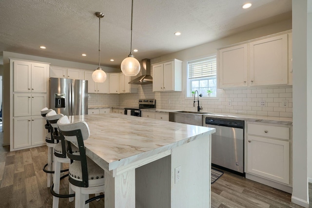 kitchen featuring sink, wall chimney range hood, a kitchen island, stainless steel appliances, and white cabinets