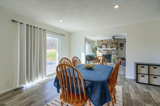 dining room with wood-type flooring, a stone fireplace, and a textured ceiling