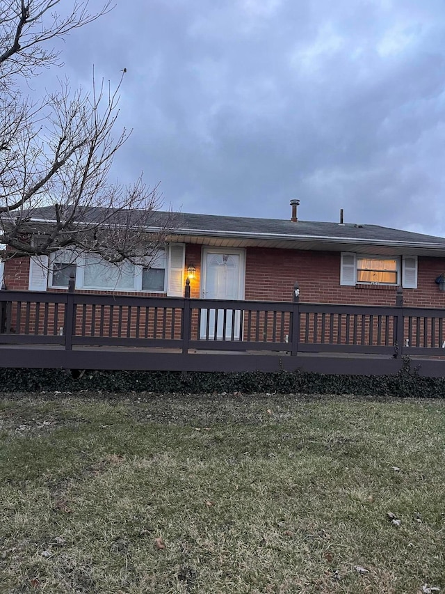 rear view of property with brick siding, a lawn, and a wooden deck