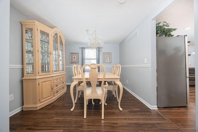 dining area with a notable chandelier, visible vents, dark wood-type flooring, a textured ceiling, and baseboards