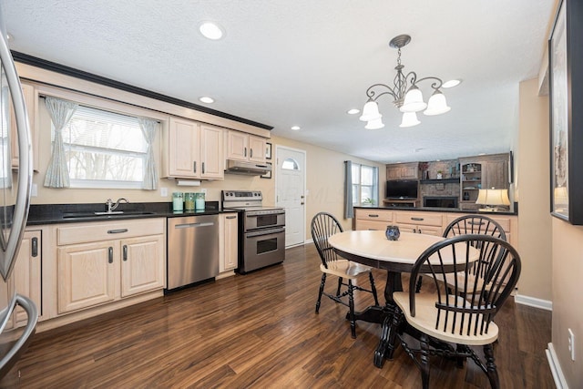 kitchen featuring under cabinet range hood, a sink, appliances with stainless steel finishes, dark countertops, and pendant lighting