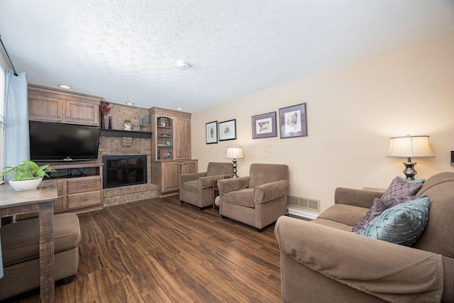 living area with a textured ceiling, a brick fireplace, dark wood finished floors, and visible vents