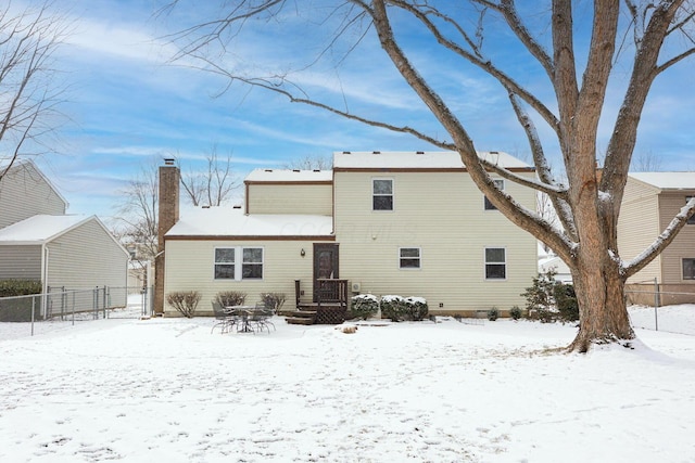 snow covered house featuring fence and a chimney